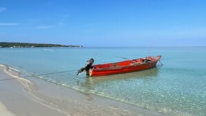 Ein rotes Boot liegt an einem Strand mit klarem Wasser und einer entfernten Küste.