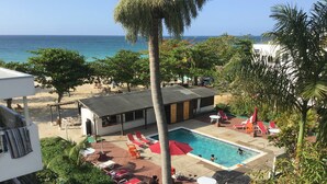 Ein Poolbereich mit Liegestühlen und einem kleinen Gebäude, umgeben von viel Grün und mit Blick aufs Meer.
