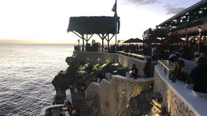 A coastal terrace with stone walls and a thatched roof structure overlooking the sea. - Beautiful Studio with Pool on Negril Beach (Negril)