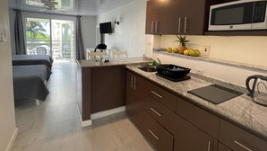 A modern kitchen with a microwave, a sink, and a countertop with a fruit bowl. There is a dining area with a table and chairs visible through a glass door. - Beautiful Studio with Pool on Negril Beach (Negril)