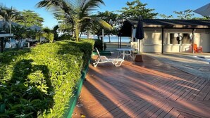 A wooden deck with lounge chairs, a covered seating area, and a view of the sea. - Beautiful Studio with Pool on Negril Beach (Negril)