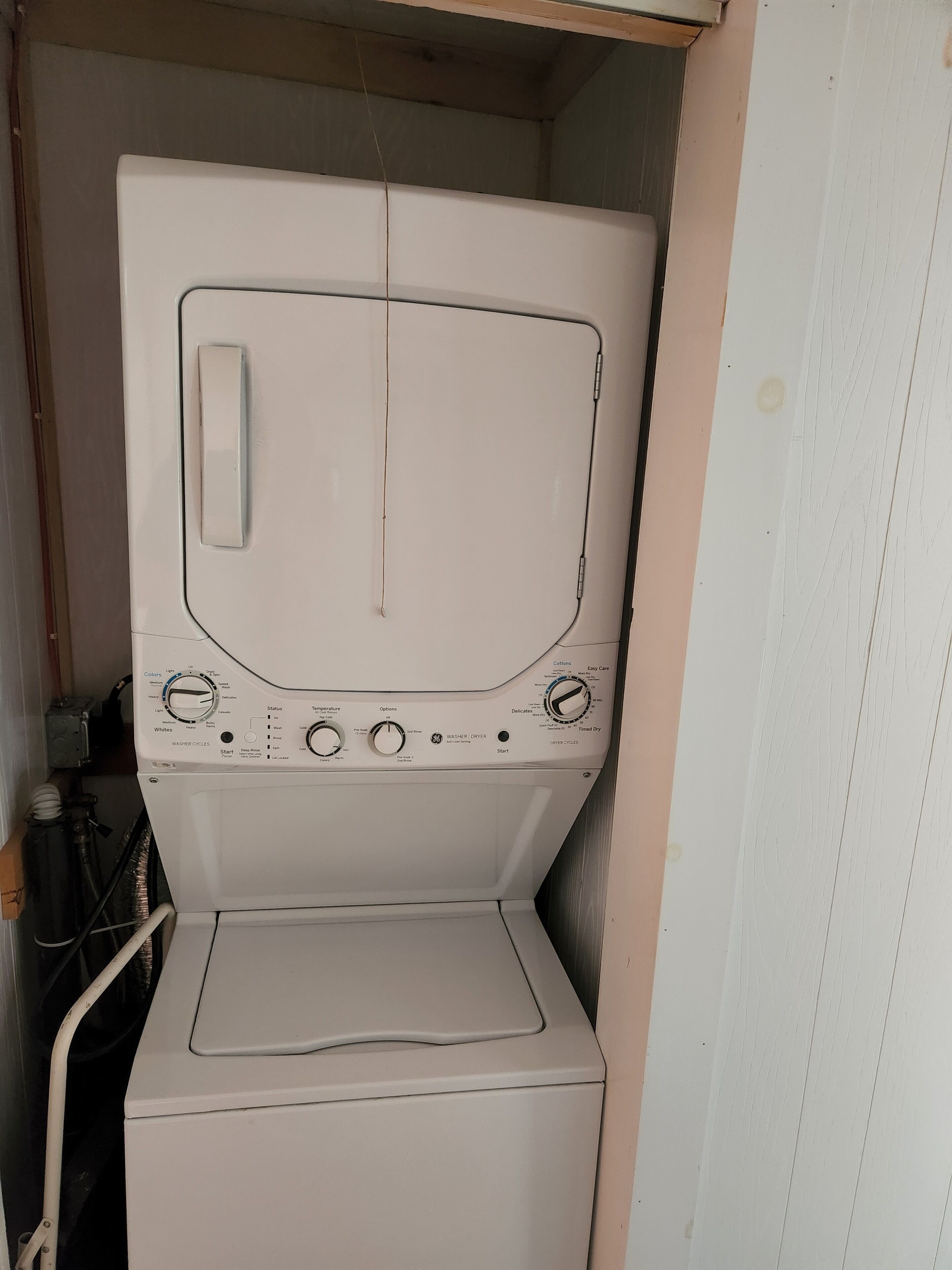 Un appareil combiné lave-linge et sèche-linge blanc et compact, doté de boutons de commande et d’une porte à chargement frontal, installé dans un petit espace clos.