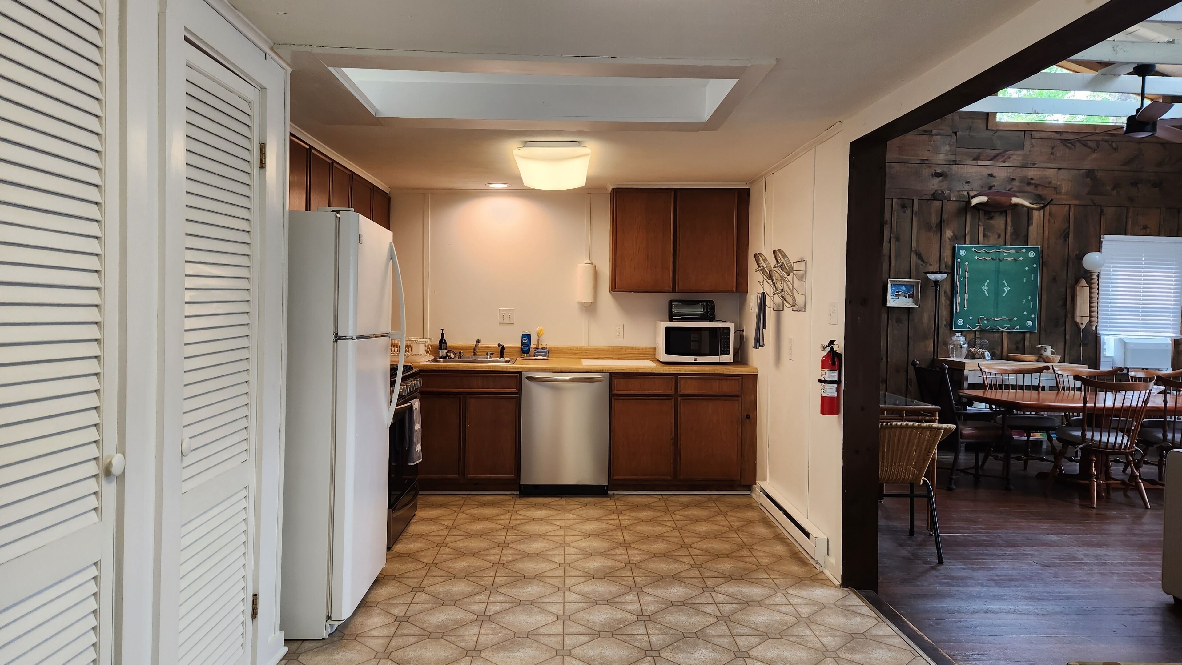 A compact kitchen with a refrigerator, microwave, and dishwasher. There is a skylight above the sink and a fire extinguisher mounted on the wall.