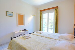 A hotel room with two beds, a bedside table, a window with curtains, and a wall-mounted picture.