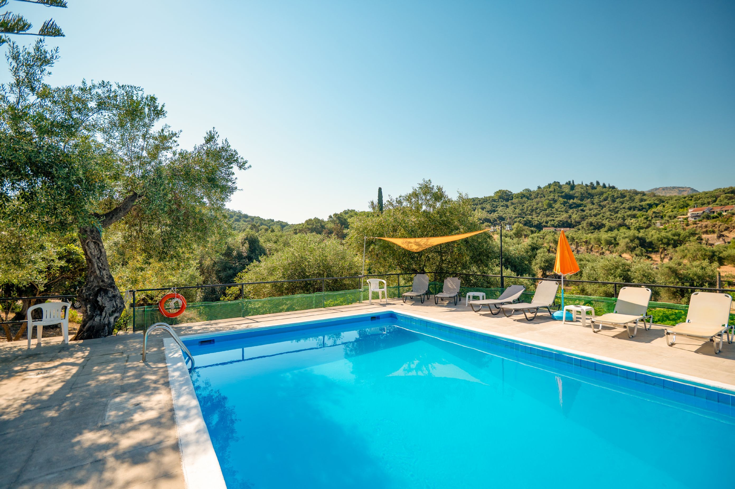A swimming pool with lounge chairs and a lifebuoy, surrounded by trees and hills.