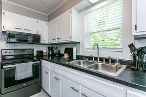 A modern kitchen with white cabinets, stainless steel appliances, a double sink, and a window with blinds.