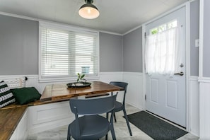 A dining area with a wooden table, two chairs, a bench, and a window with blinds.