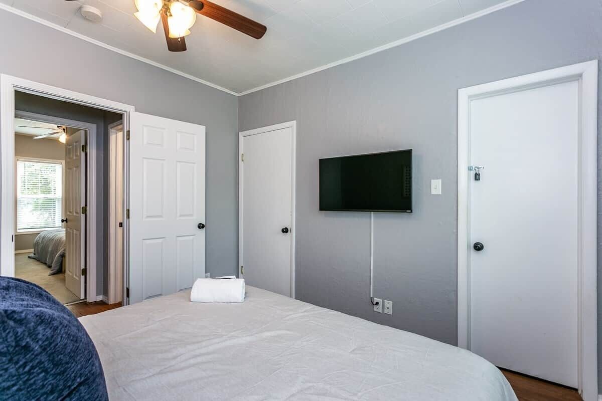 A bedroom with a bed, a television mounted on the wall, and a ceiling fan.