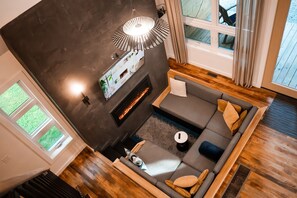 Un salon moderne avec une cheminée, un ensemble de canapés, une table basse et une grande fenêtre avec des rideaux.