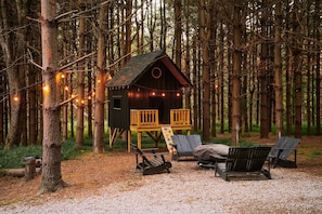 A wooden cabin with a deck, surrounded by trees, and furnished with outdoor seating.
