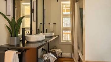 A bathroom with a large mirror, two sinks, a potted plant, and a window with curtains.