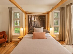 Une chambre avec un grand lit, deux tables de chevet, une chaise et une fresque murale sur le thème de la forêt.