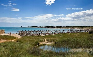 Ein Strand mit Liegestühlen und Sonnenschirmen, einem klaren Himmel und einem Gewässer.