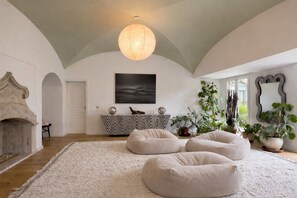 Un salon spacieux avec un plafond haut, une cheminée, un grand canapé, une console agrémentée d’objets décoratifs et une variété de plantes.