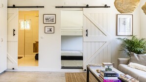 Ein modernes Wohnzimmer mit Sofa, Couchtisch mit Büchern, einer Pendelleuchte und einer Treppe, die in ein Schlafzimmer führt.
