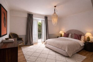 Een slaapkamer met een bed, nachtlampjes, een stoel, een bureau en een schilderij.