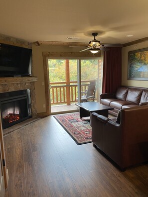 Relax in this inviting living room with a fireplace, sofa, and TV, offering a view of the surrounding landscape from the large window.