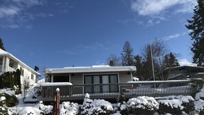 Una casa moderna con un portico coperto, un paesaggio innevato e un cielo azzurro limpido.