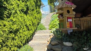 Un sentiero stretto costeggiato da fitta vegetazione verde, conduce a un edificio rustico con tetto di paglia.
