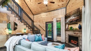 L’intérieur d’un chalet confortable, avec un escalier, une cheminée, un canapé et un téléviseur.