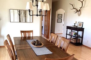 A dining room with a wooden table, chairs, a chandelier, a wall-mounted deer skull, and a bookshelf. - Mountain -Ranch Views! Near River Access! Fly Fishing. (Salida)