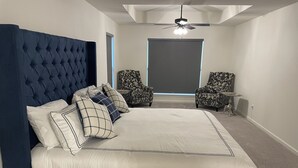 Ein Schlafzimmer mit einem großen Bett, zwei gemusterten Sesseln, einem Deckenventilator und einer Projektionsleinwand.