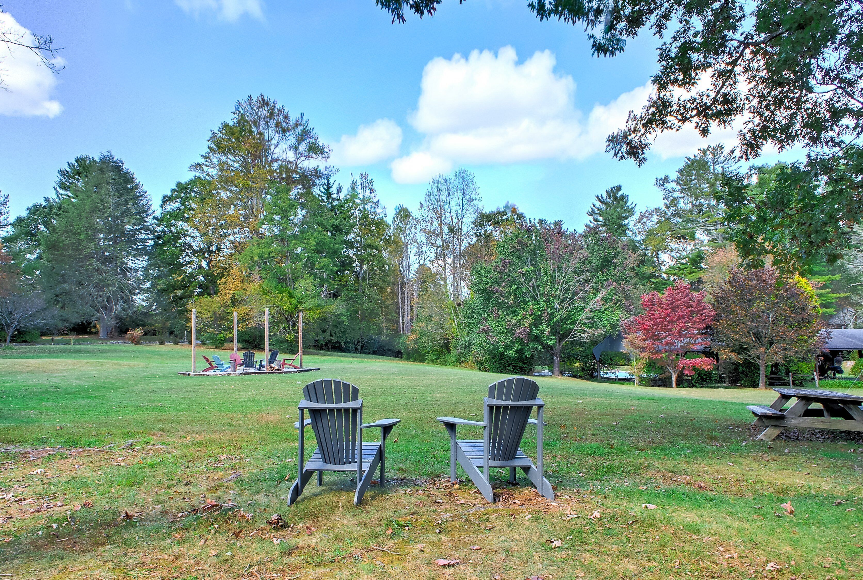 A grassy outdoor area with two Adirondack chairs facing a picnic table.