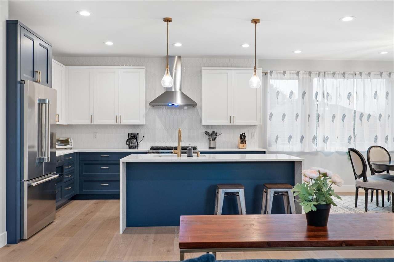 A modern kitchen with white cabinets, a central island, stainless steel appliances, pendant lighting, and a dining area with a wooden table and chairs.
