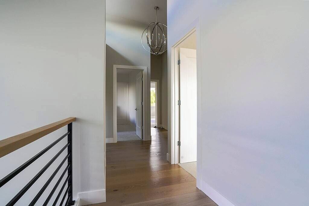 A hallway with wooden flooring, white walls, and a black railing.
