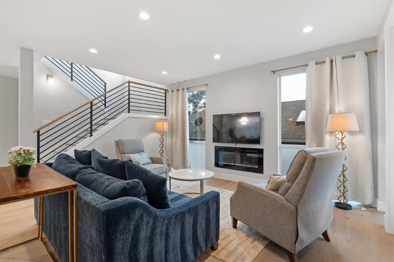 A modern living room with a blue sectional sofa, a beige armchair, a small round coffee table, a TV, and a staircase.