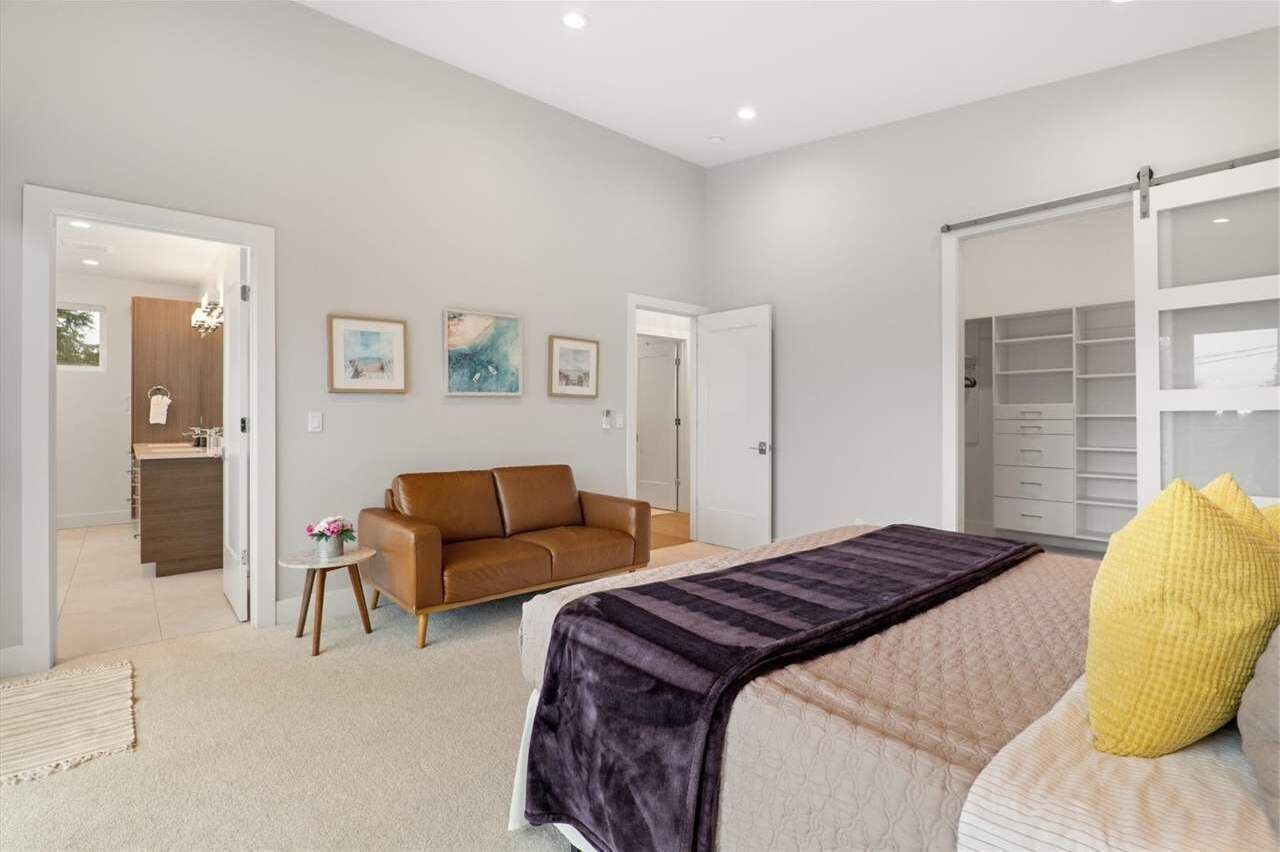 A bedroom with a bed, a brown leather sofa, a small table with flowers, and a closet with open doors.