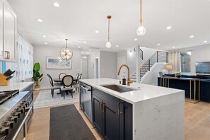 A modern kitchen with a central island, a dining area with a round table, and a staircase leading to an upper level. - New House with Chef's Kitchen and Spa-like Suite (Seattle)
