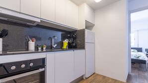 Una cucina moderna con mobili bianchi, un piano di lavoro nero, forno integrato, macchina per il caffè e frigorifero.