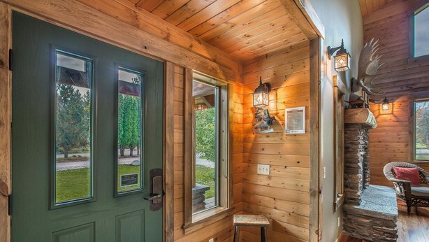 Interior de una cabaña de madera con una puerta verde, un banco de piedra y una decoración de cabeza de ciervo.