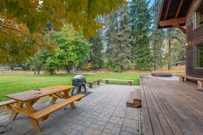 Una terraza de madera con mesas de picnic y una parrilla.