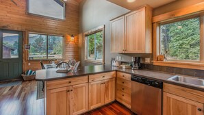 Una cocina moderna con armarios de madera, lavavajillas y ventanas amplias que ofrecen vistas al exterior.