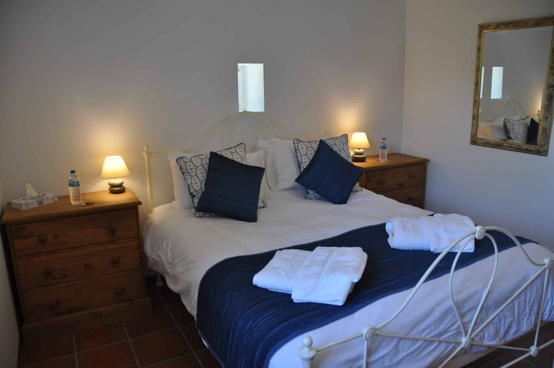A hotel room with a bed, two bedside tables, a mirror, and a wooden dresser.