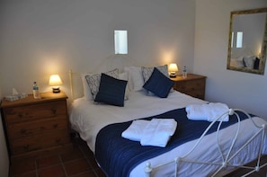 Quarto de hotel com uma cama, duas mesas de cabeceira, um espelho e uma cômoda de madeira.