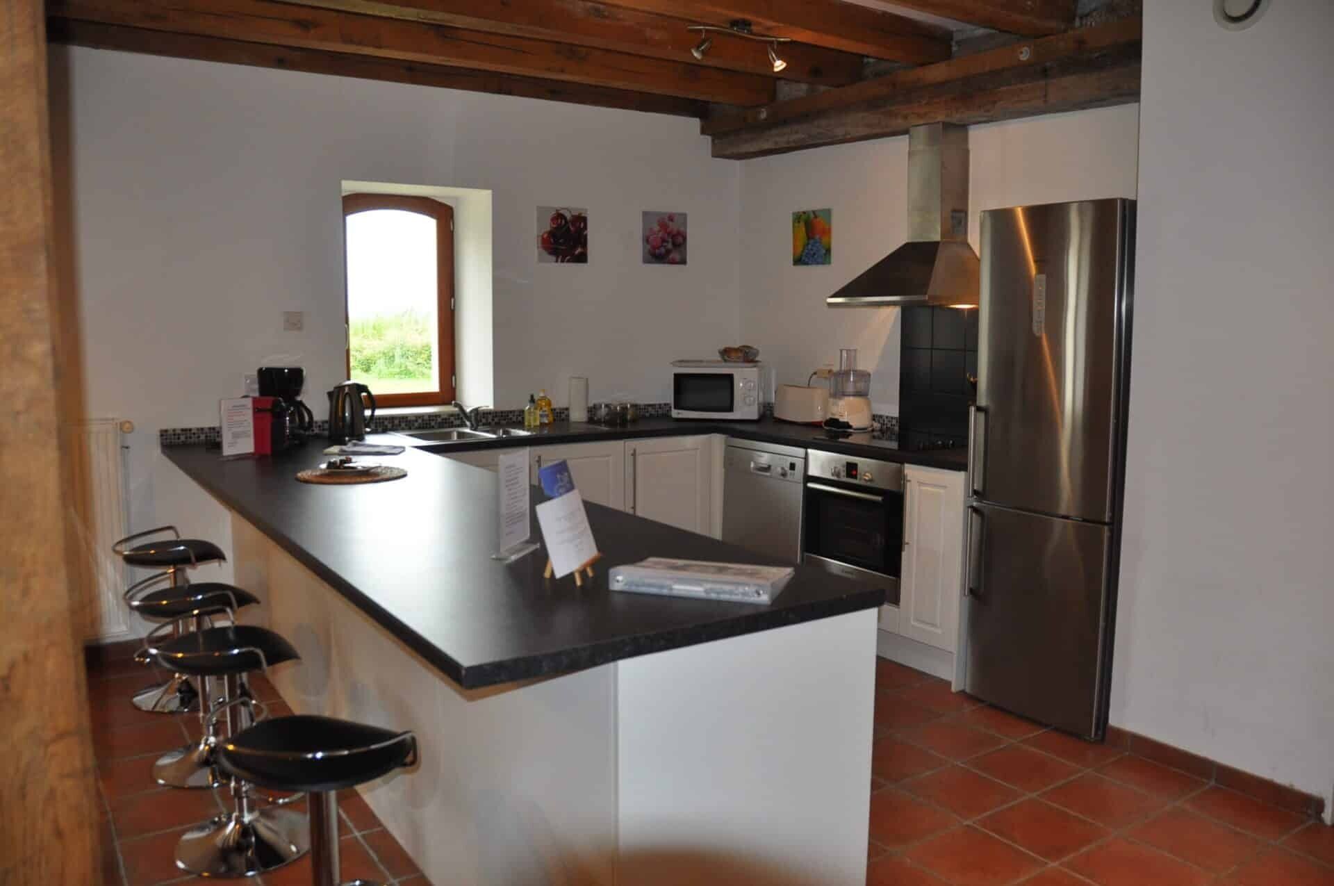 Una cocina con una isla central, taburetes de bar, un refrigerador, un microondas y un ventanal.