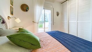 Un dormitorio con cama, mesita de noche, lámpara, ventana con cortinas y vistas al exterior.