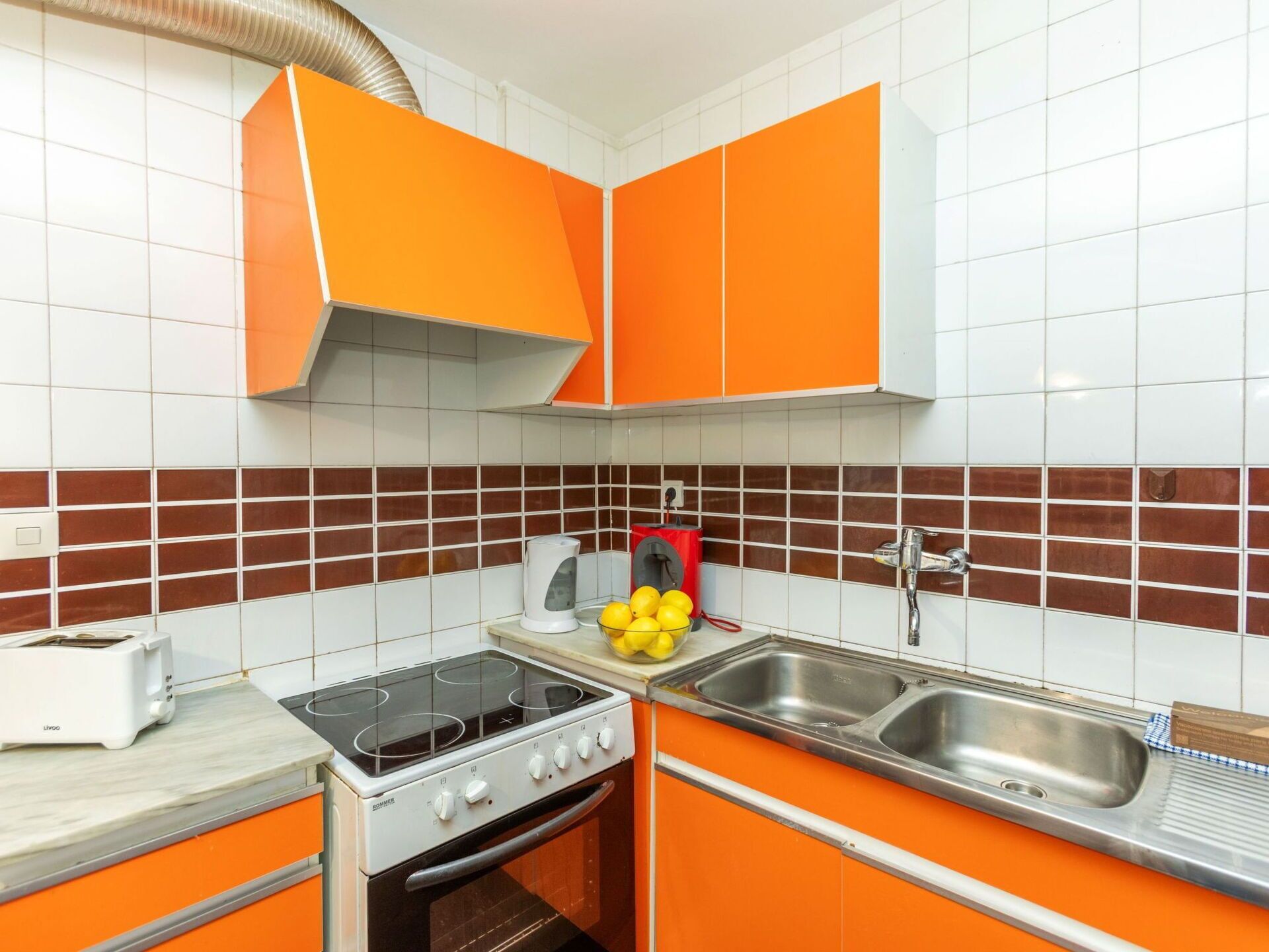 Een keuken met oranje kastjes, een fornuis, een spoelbak en een broodrooster.