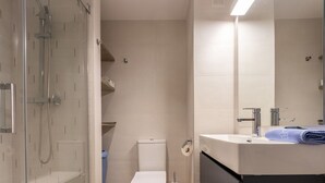 Un baño moderno con ducha envuelta en vidrio, inodoro y lavamanos con una toalla.