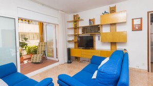 Una sala de estar con sofás azules, un televisor, estanterías de madera y un ventanal corredero que da a un espacio exterior.