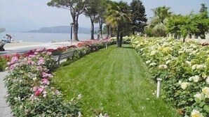 A pathway lined with flowering plants and trees, leading to a beach. - Residence Florida B10 - 200m from the lakefront (Lazise)