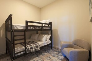A bunk bed with a checkered throw blanket, a chair, and a plain wall.