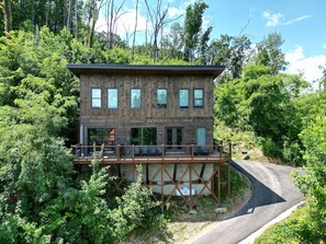 Une cabane en bois à deux étages, dotée d’une terrasse et entourée d’une forêt dense.