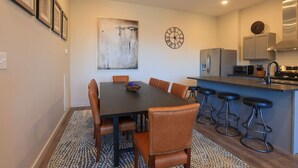 Une cuisine moderne avec une table à manger, des chaises, des tabourets de bar et une horloge au mur.