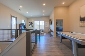 A spacious room with a pool table, a gaming console, and a staircase.