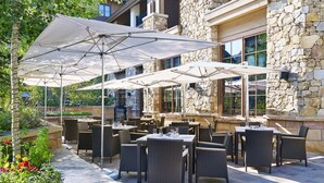 An outdoor patio area with tables and chairs, stone walls, and large umbrellas providing shade. - The Sebastian Vail 2 Bedroom Residence (Vail)