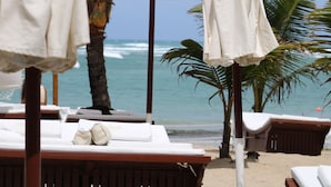 Habitación de hotel frente a la playa, con cama de madera, ropa de cama blanca y vista al océano.